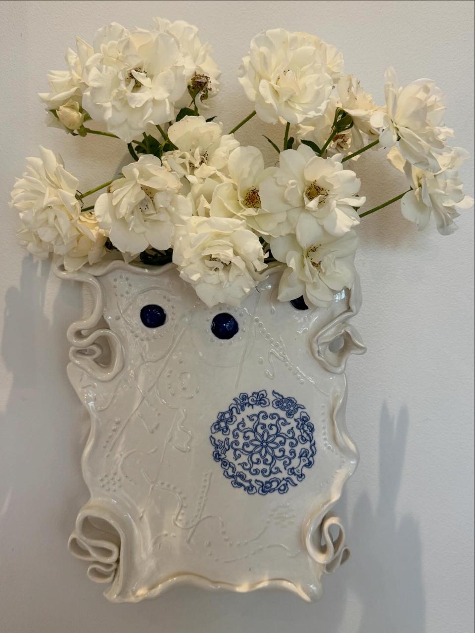 A hand-built porcelain wall vase holding white roses